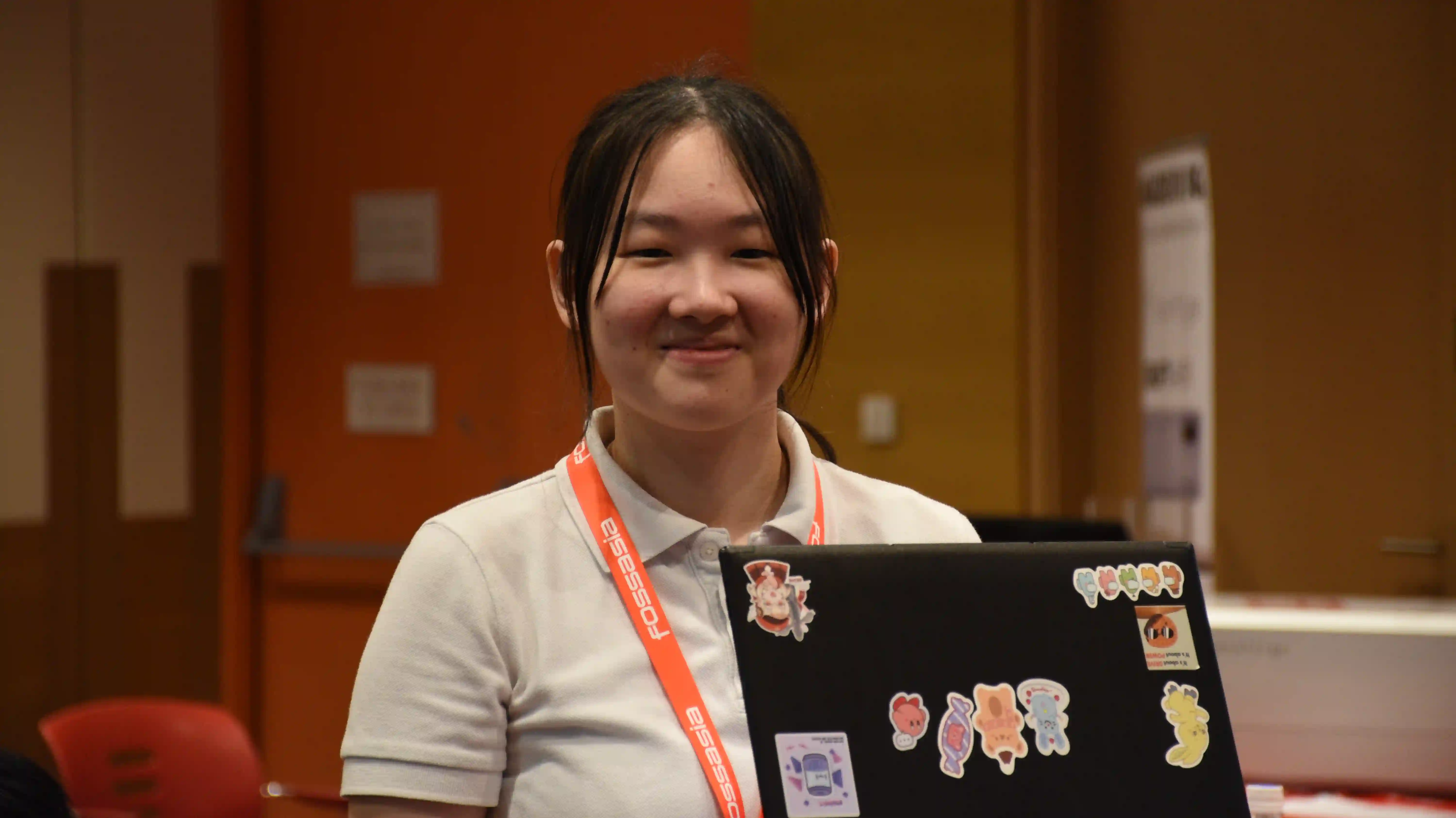 An image of a lady with a FossAsia lanyard holding a laptop in a auditorium